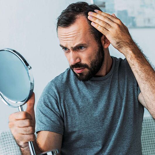 Mann mit Spiegel in der Hand, der seine Haaren Haarwuchs kontrolliert